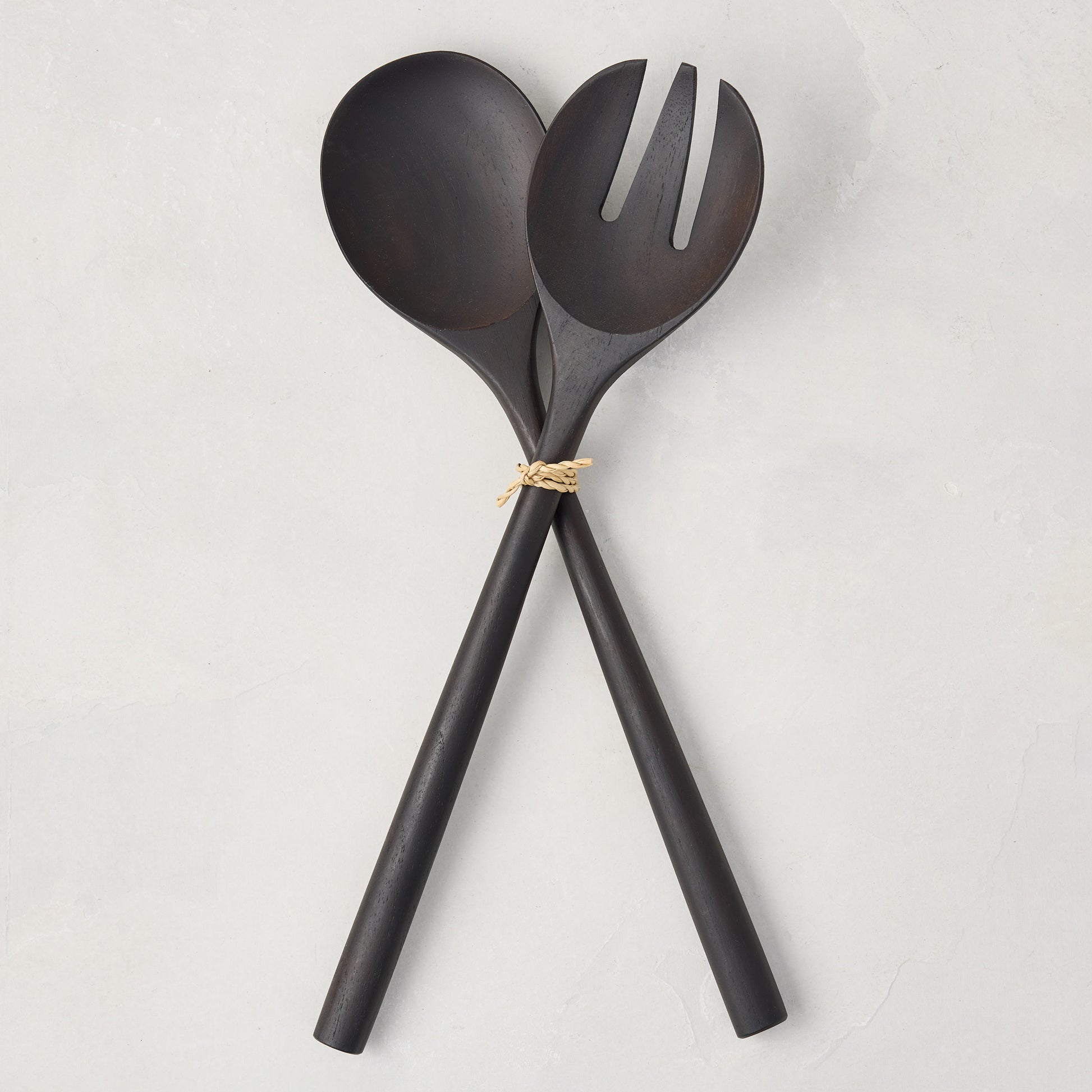 Ebony teak wood long-handled 2-piece serving set, spoon and fork, tied with twine on a white background.
