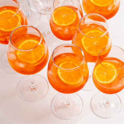 Elijah Large Scissor-Cut Wine Glass filled with orange cocktail and a citrus slice.