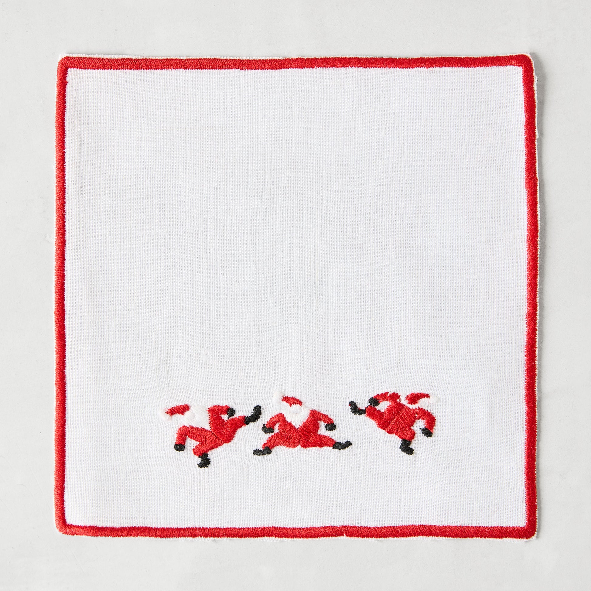 White linen coaster with red embroidered Santa figures and a red border.