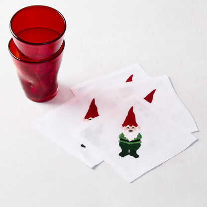Set of 4 white linen 5.5" square cocktail napkins with embroidered gnomes in red hats and green outfits.