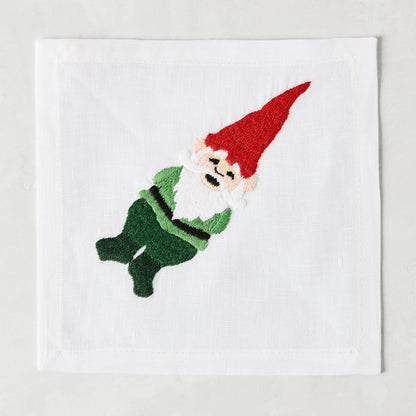 White linen cocktail napkin coaster with embroidered gnome in red hat and green outfit.