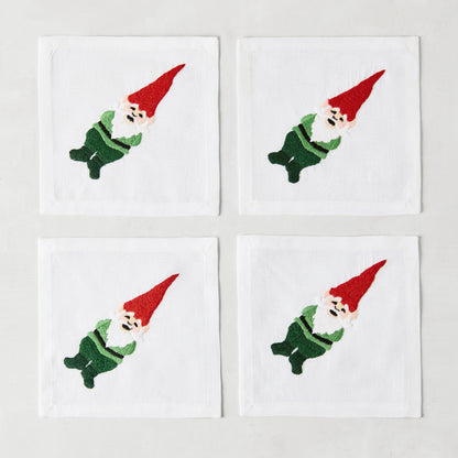 Set of 4 white linen 5.5" square cocktail napkins with embroidered gnomes in red hats and green outfits.