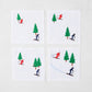 Set of 4 white linen coasters with embroidered skiers in red and blue, and green trees.