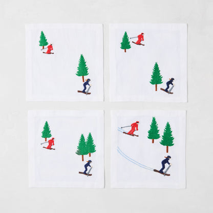 Set of 4 white linen coasters with embroidered skiers in red and blue, and green trees.