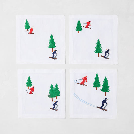 Set of 4 white linen coasters with embroidered skiers in red and blue, and green trees.