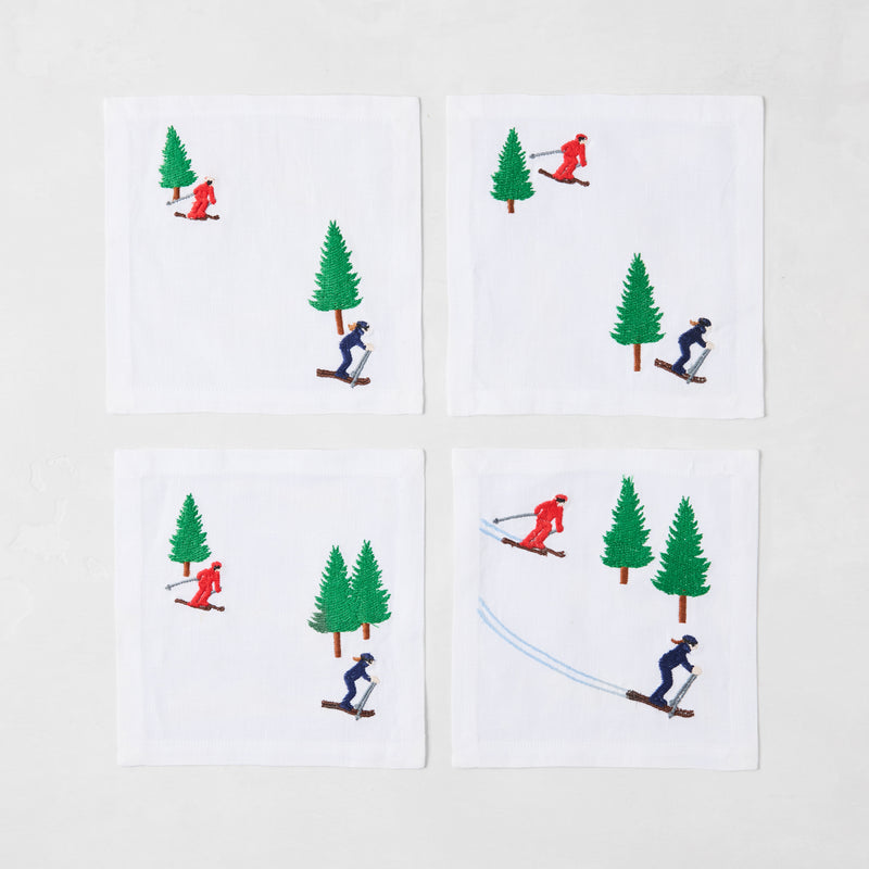 Set of 4 white linen coasters with embroidered skiers in red and blue, and green trees.