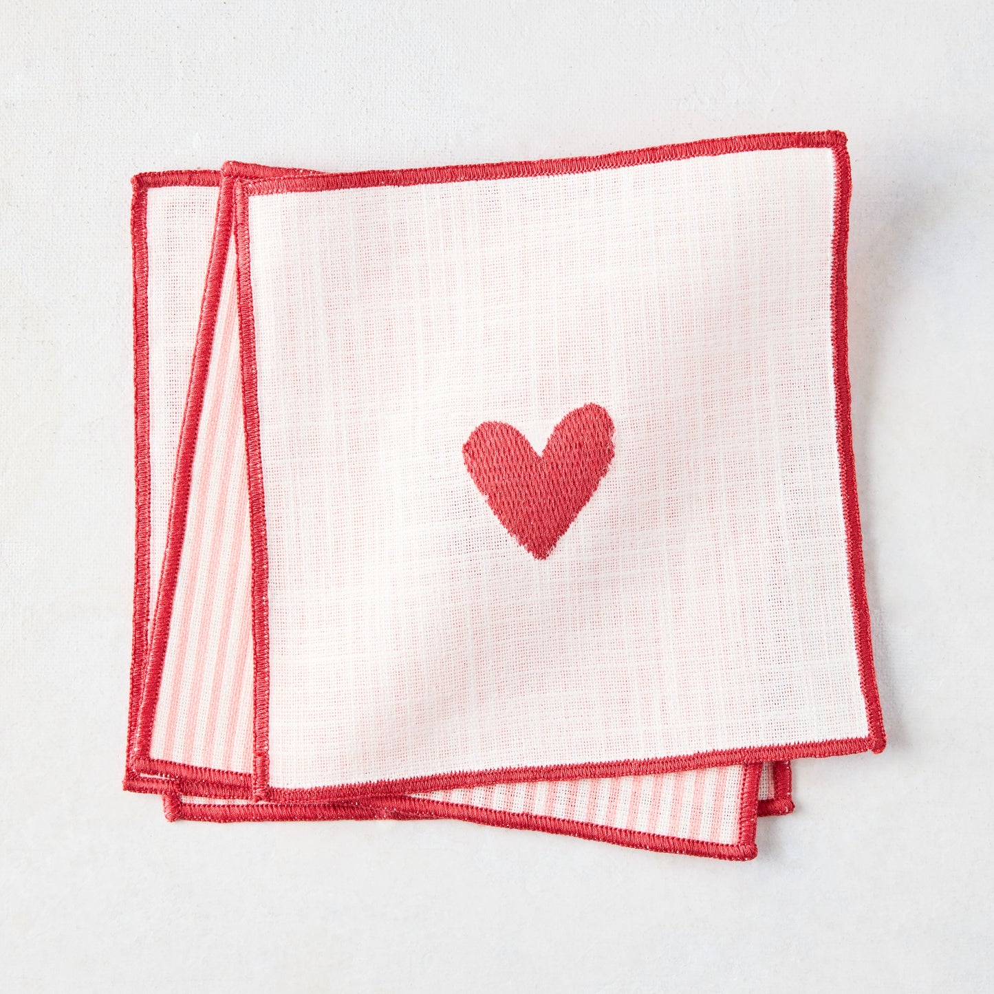Set of 4 cotton coasters with red embroidered heart and striped edge on pale pink and white.