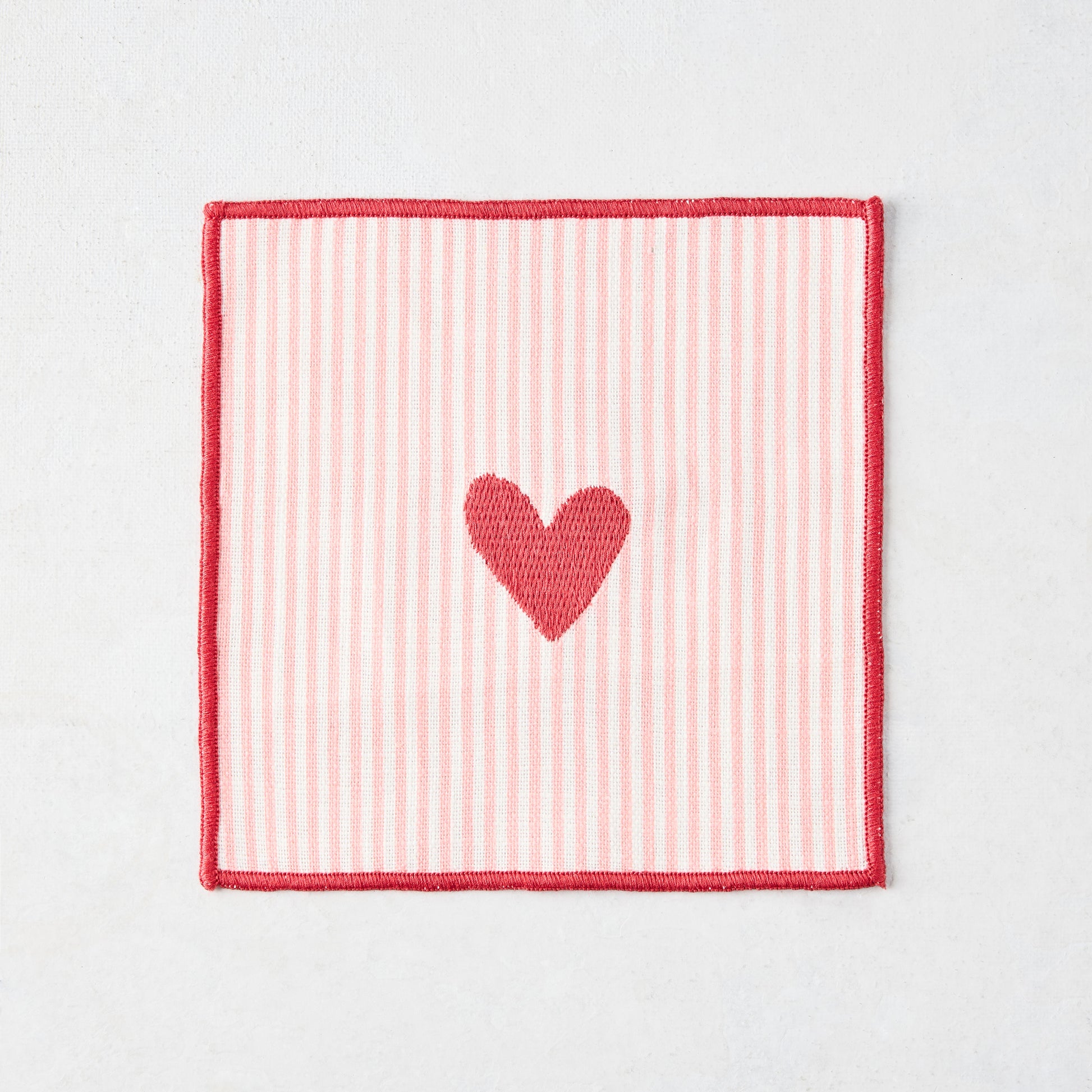 Cotton coaster with pale pink and white stripes, red embroidered heart, and red edge.