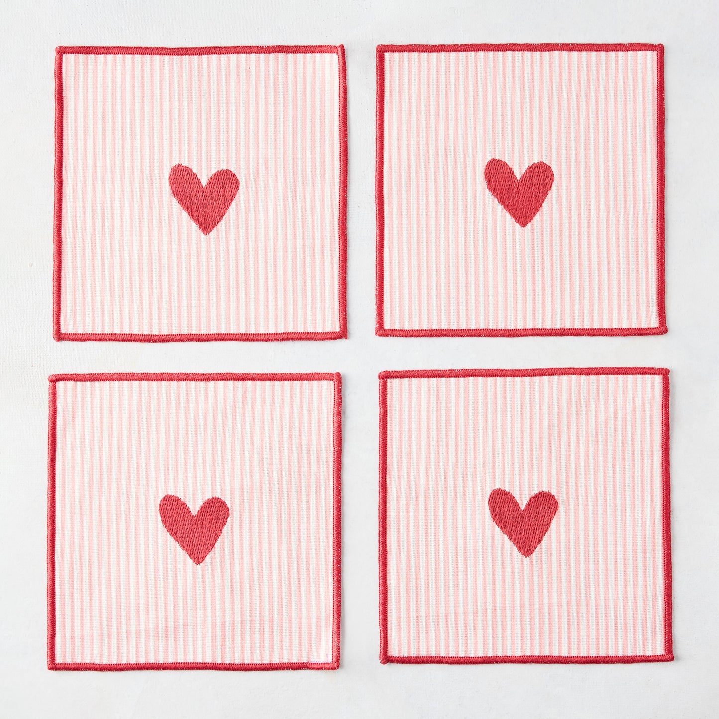 Set of 4 square cotton coasters with pale pink and white stripes, red embroidered hearts, and red edges.