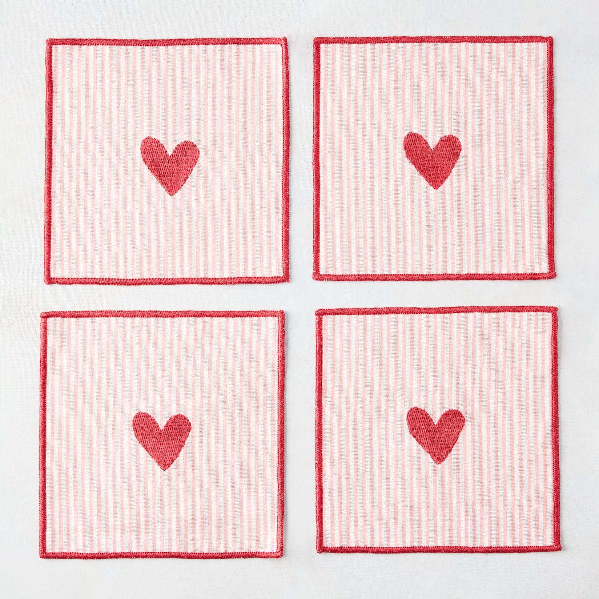 Set of 4 square cotton coasters with pale pink and white stripes, red embroidered hearts, and red edges.