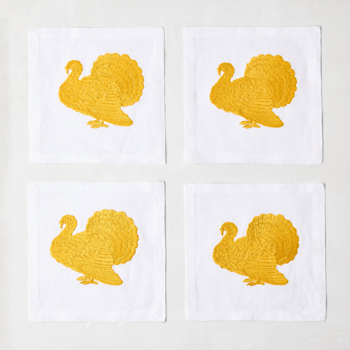 Set of four 5.5-inch white linen cocktail napkins featuring gold embroidered turkey designs.