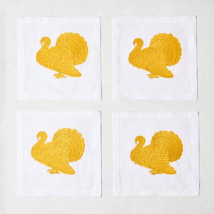 Set of four 5.5-inch white linen cocktail napkins featuring gold embroidered turkey designs.