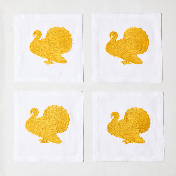 Set of four 5.5-inch white linen cocktail napkins featuring gold embroidered turkey designs.