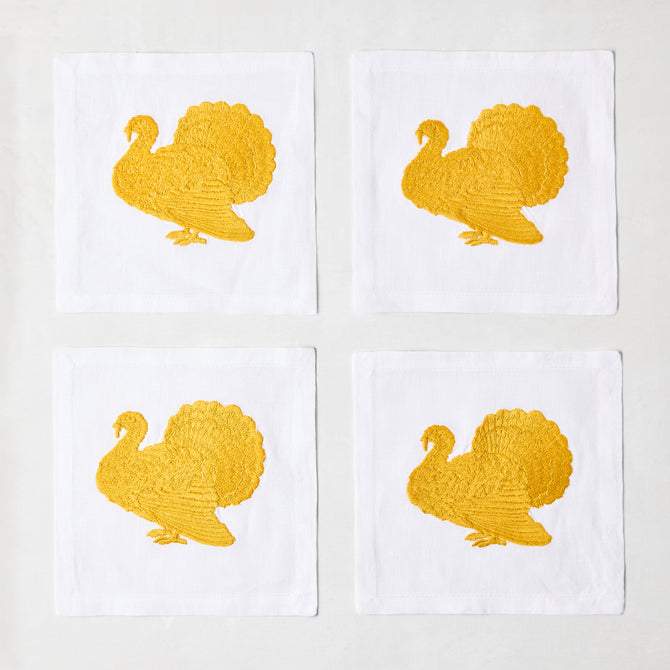 Set of four 5.5-inch white linen cocktail napkins featuring gold embroidered turkey designs.
