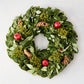 24-inch holiday wreath featuring magnolia leaves, fir, boxwood, pinecones, and red pomegranates on a light background.