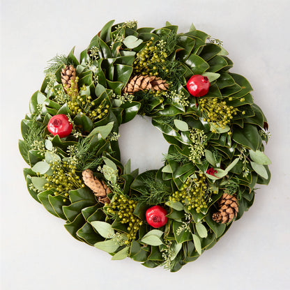 24-inch holiday wreath featuring magnolia leaves, fir, boxwood, pinecones, and red pomegranates on a light background.