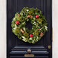 24-inch holiday wreath featuring magnolia leaves, boxwood, fir, pinecones, and red pomegranates on a black door.