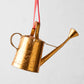 Gold metal watering can Christmas tree ornament with red ribbon.