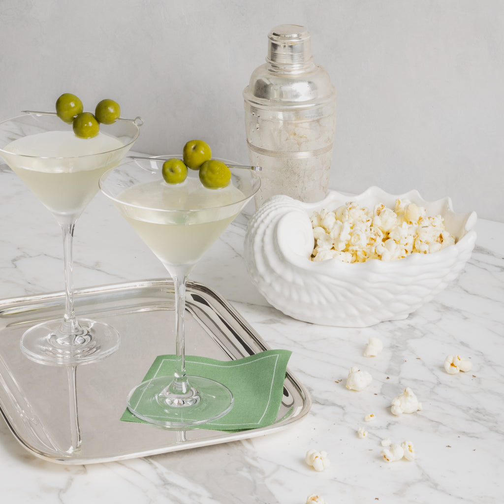Green eucalyptus tear-off cotton cocktail napkin under a martini glass on a silver tray.