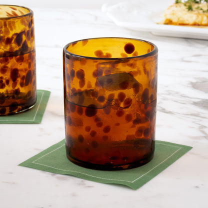 Amber tortoise shell drinking glass with ice on a green square coaster.