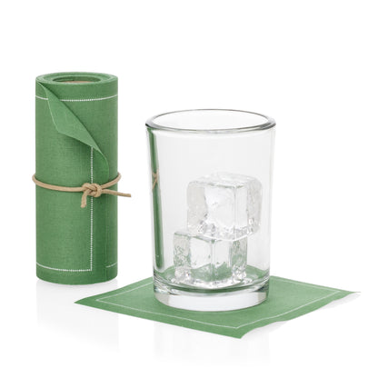 Roll of 50 eucalyptus green cotton cocktail napkins with white stitching, tied with twine, next to a glass with ice on a single napkin.