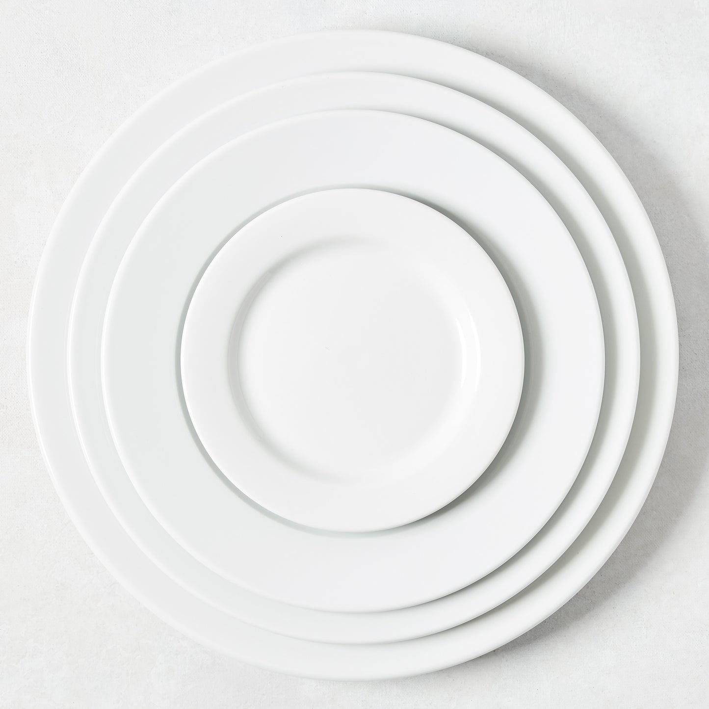 Stack of four white porcelain dinner plates with classic rims, varying in size.
