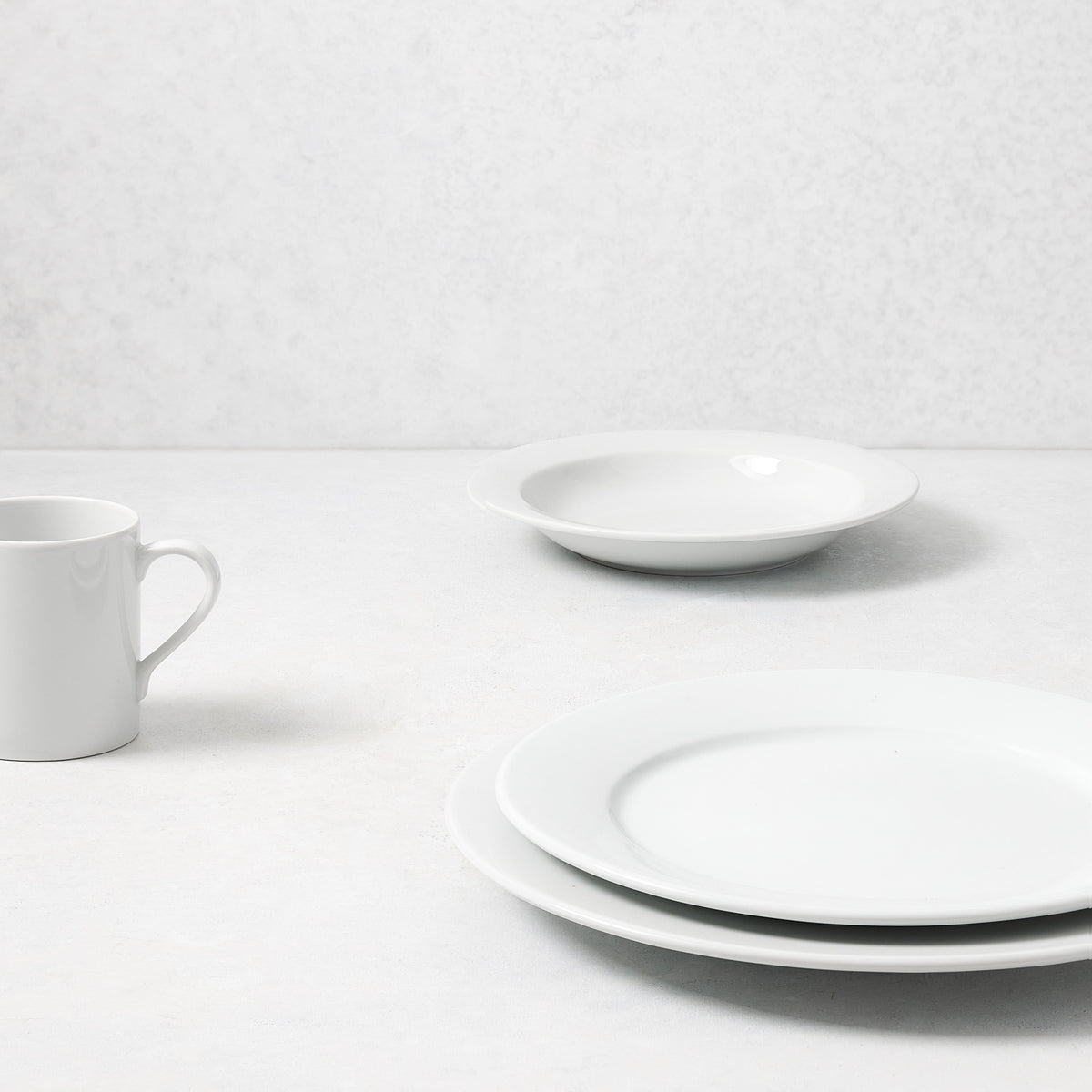 Everyday porcelain mug and dinnerware set in glossy white, featuring a classic rim design on a neutral background.