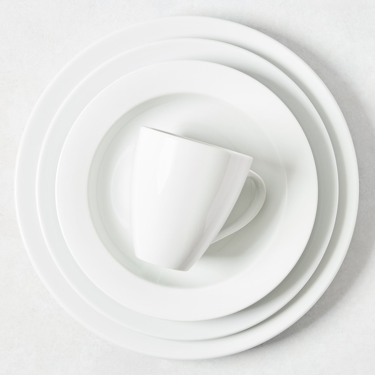 Stacked white porcelain dinnerware: mug, salad plate, and two larger plates from the Everyday collection.