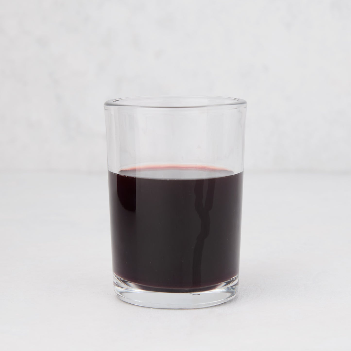 Clear, simple Hudson Grace Everyday Wine Glass filled with red liquid on a white background.