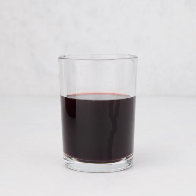 Clear, simple Hudson Grace Everyday Wine Glass filled with red liquid on a white background.