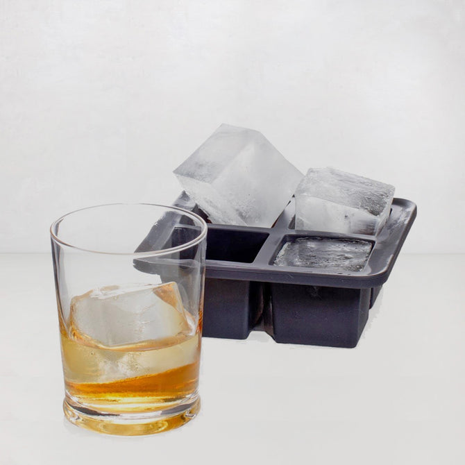 Dark gray silicone ice cube tray with four large cubes, one in a whiskey glass.