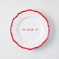7-inch white ceramic appetizer plate with a scalloped red rim and hand-painted multicolored Fa La La La text.