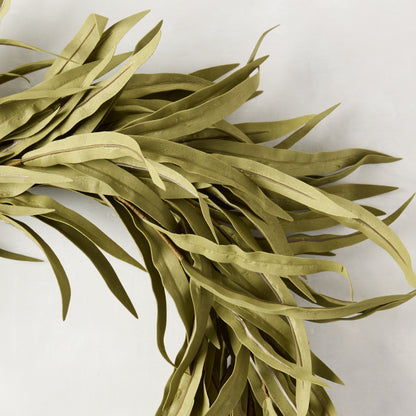 Close-up of a 12" faux willow wreath with long, muted green plastic leaves on a white background.