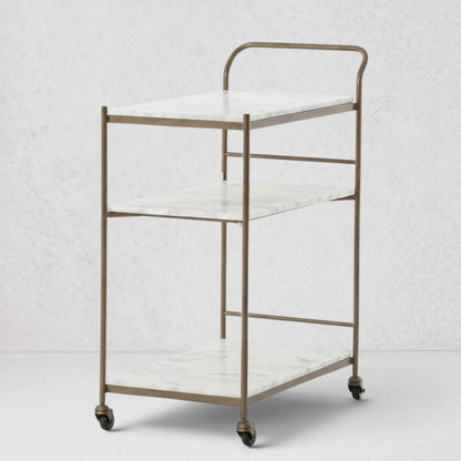 Felix antique brass bar cart with three white marble rectangular shelves on casters.