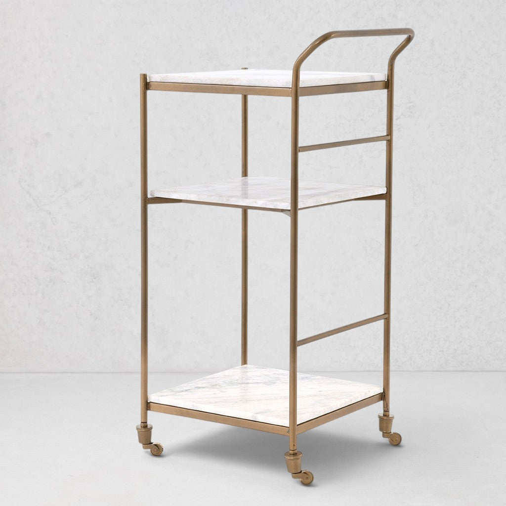 Felix antique brass bar cart with three square white marble shelves and casters.