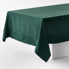 Hand-dyed fir green linen tablecloth with mitered corner detailing draped over a white table.