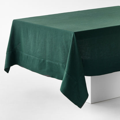 Hand-dyed fir green linen tablecloth with mitered corner detailing draped over a white table.