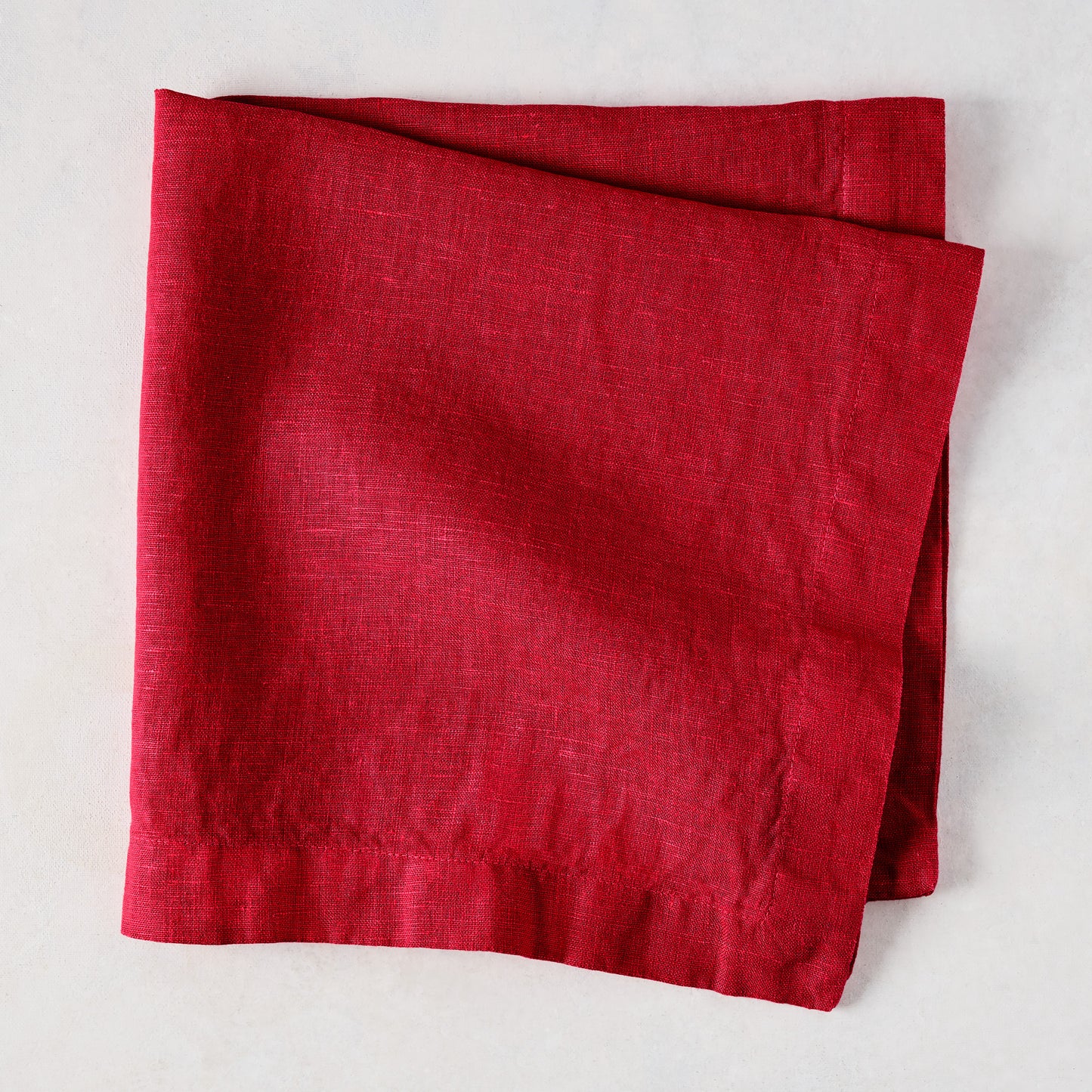 Flame HG Signature hand-dyed 22" square linen napkin in vibrant holiday red, folded on a light surface.