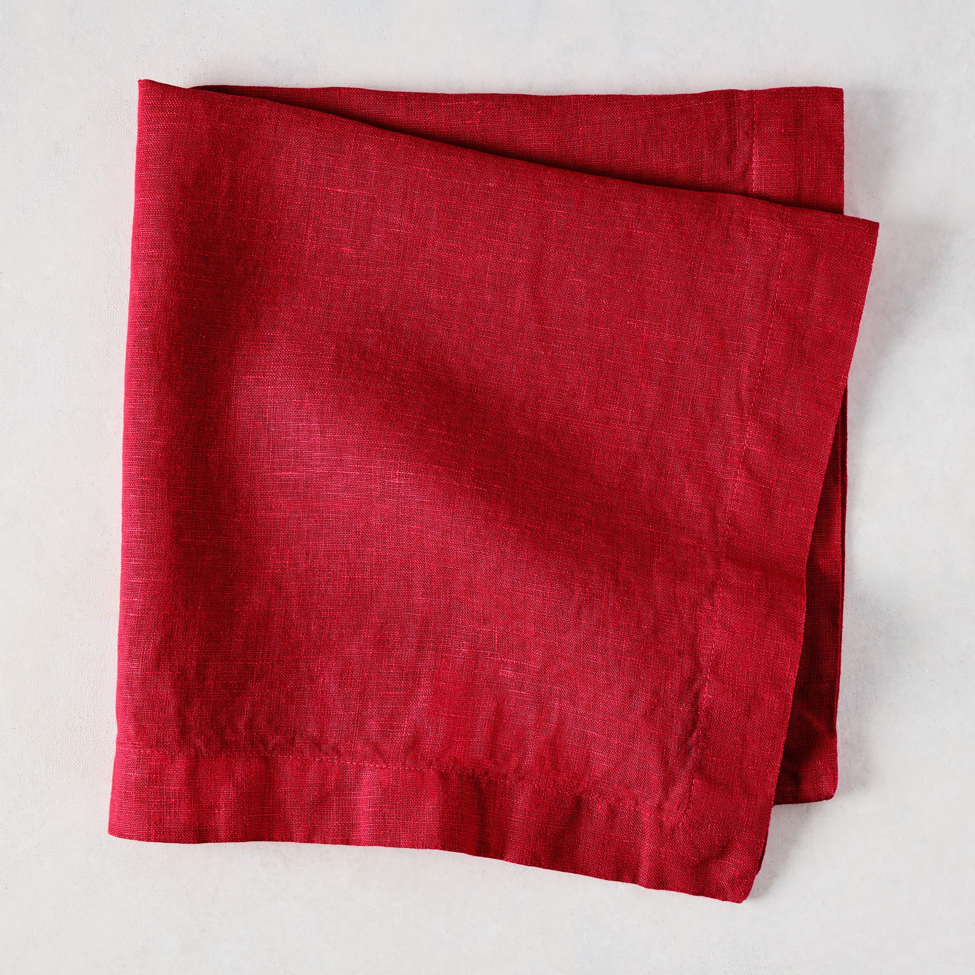 Flame HG Signature hand-dyed 22" square linen napkin in vibrant holiday red, folded on a light surface.