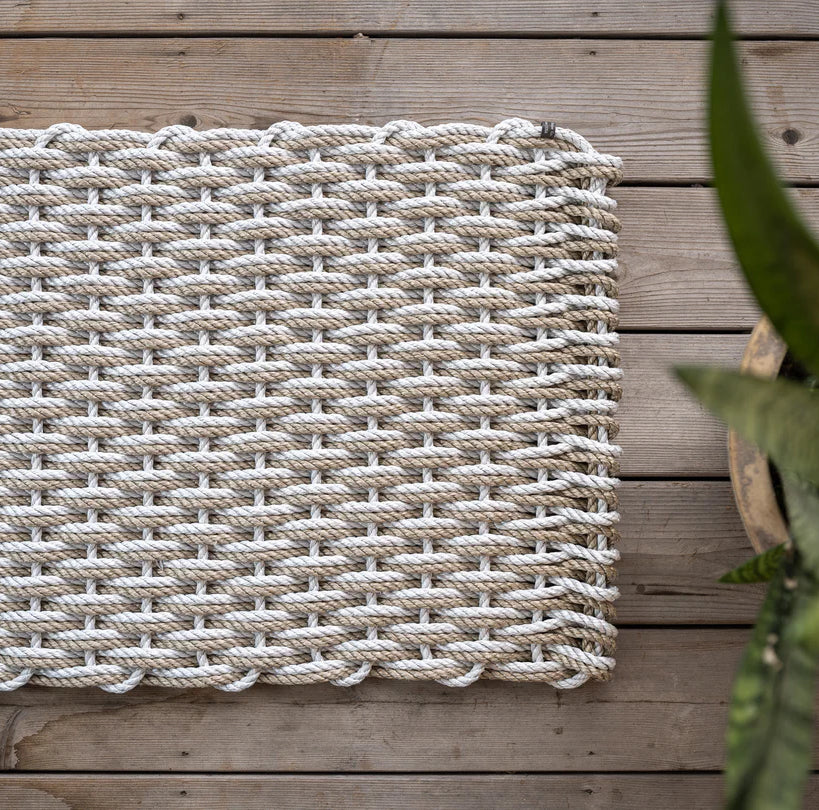 Handwoven Fog Grey and Sand Rope Doormat on a wooden deck, with a potted plant visible.