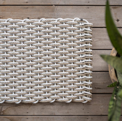 Handwoven Fog Grey and Sand Rope Doormat on a wooden deck, with a potted plant visible.