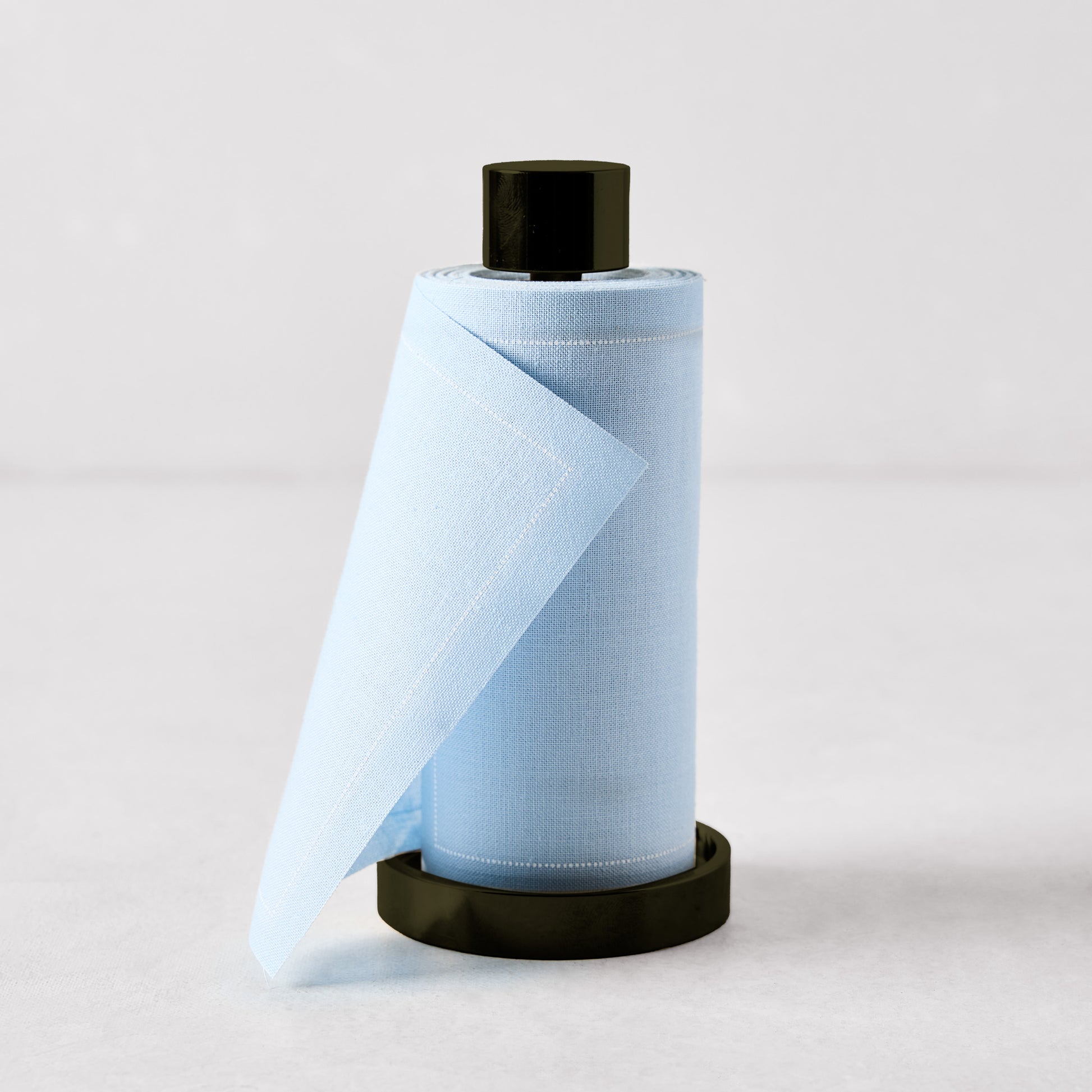 Foggy blue cotton tear-off napkins on a black metal holder, 5-inch height, minimalist bar accessory.