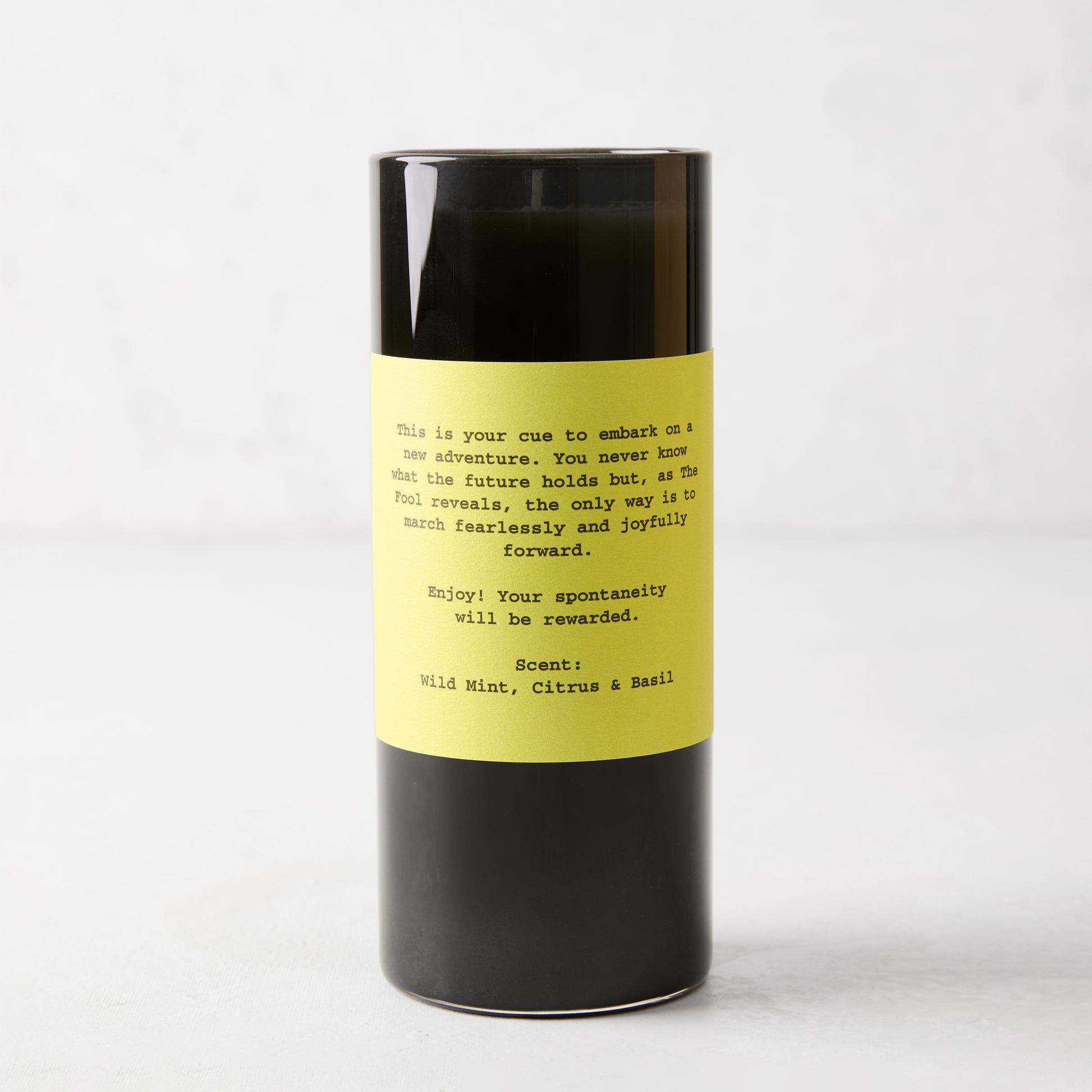 Tall black soy wax candle in a glass jar with a yellow label featuring The Fool Tarot reading and scent notes.