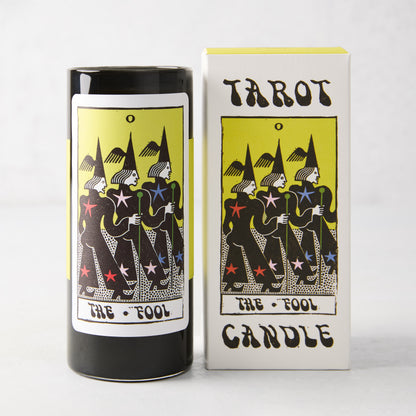 Black cylindrical soy candle and white box featuring The Fool tarot card illustration with yellow, black, and star accents.