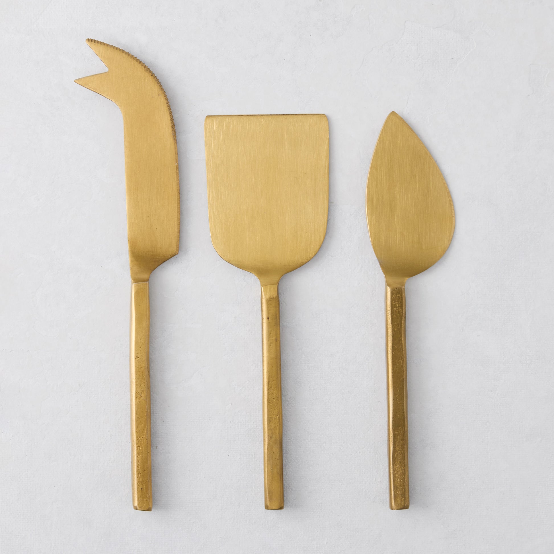 Forged gold 3-piece stainless steel cheese knife set with hammered texture and slender square handles.