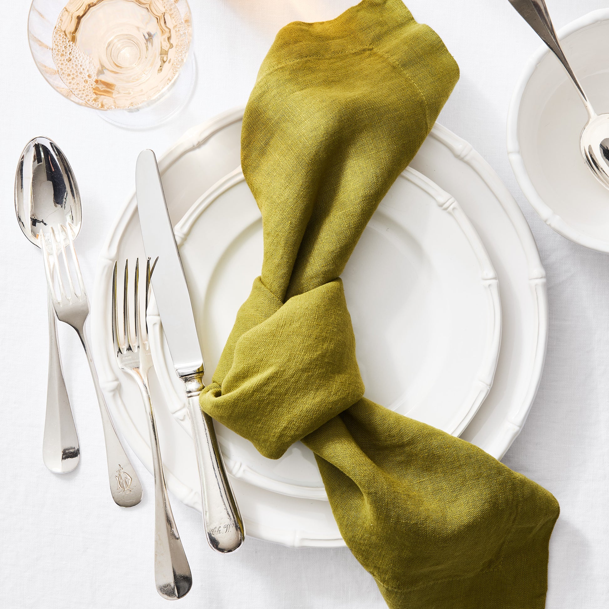 Vintage French silverplate fork and spoon set with intricate detailing on white plates and a green linen napkin.