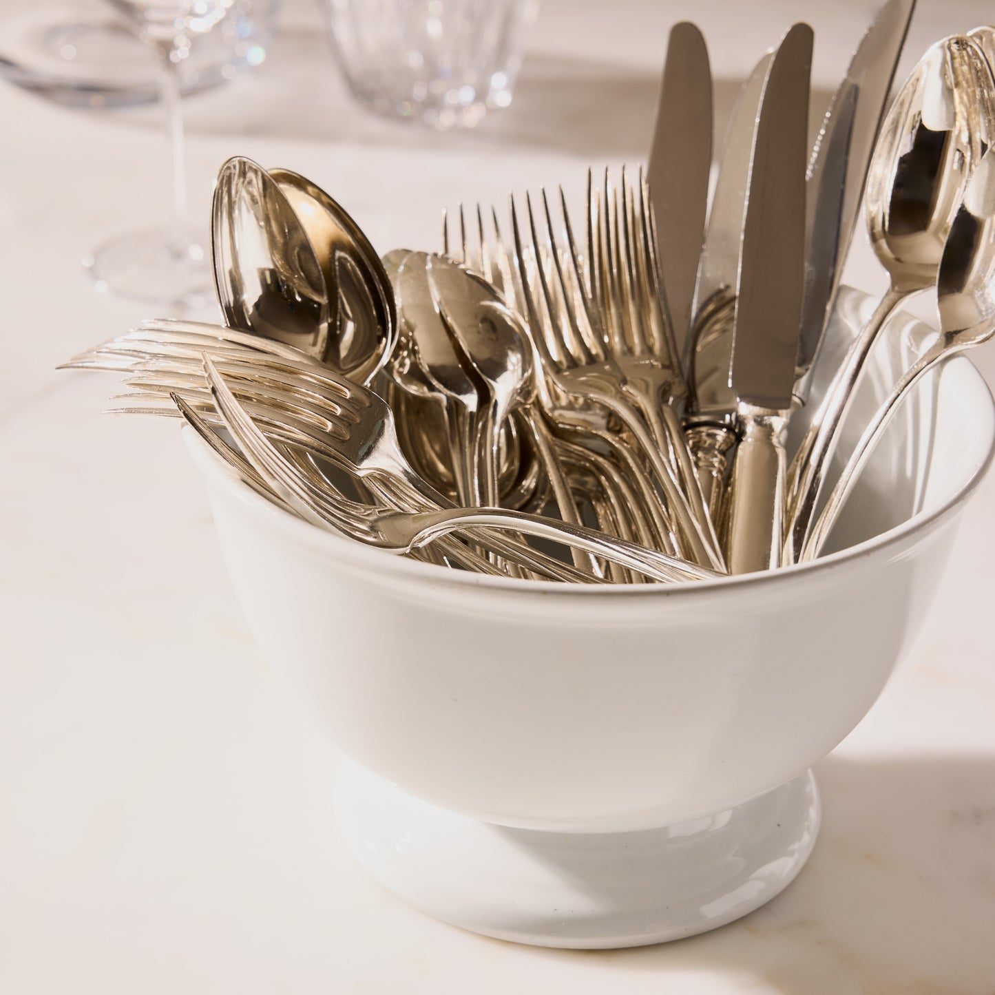 Set of 12 vintage French silver spoons and forks with intricate detailing in a white ceramic bowl.