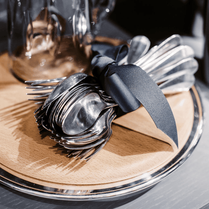 Vintage French silverplate flatware set, spoons and forks tied with a dark ribbon on a wooden tray.