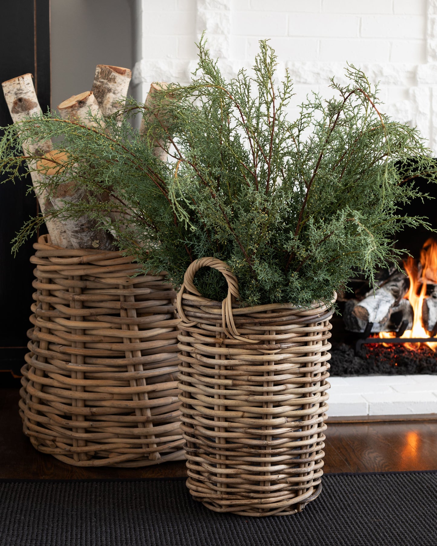 Fresh Carolina Sapphire greenery stems in a tall woven wicker basket next to a fireplace.