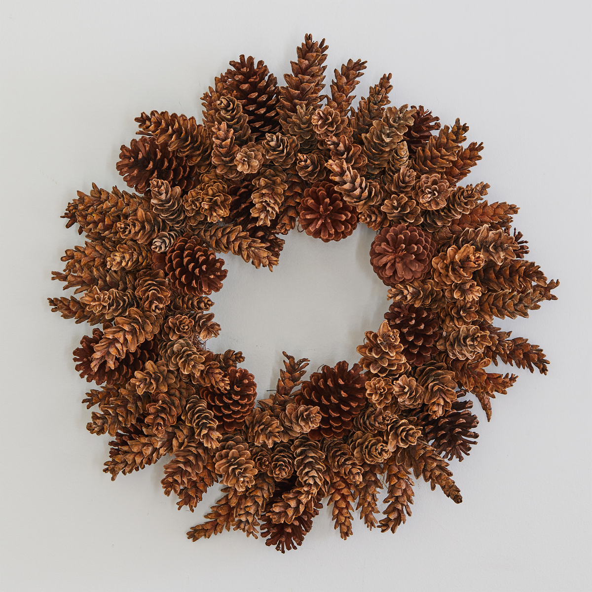 Handmade holiday wreath crafted from natural brown pinecones on a plain white background.